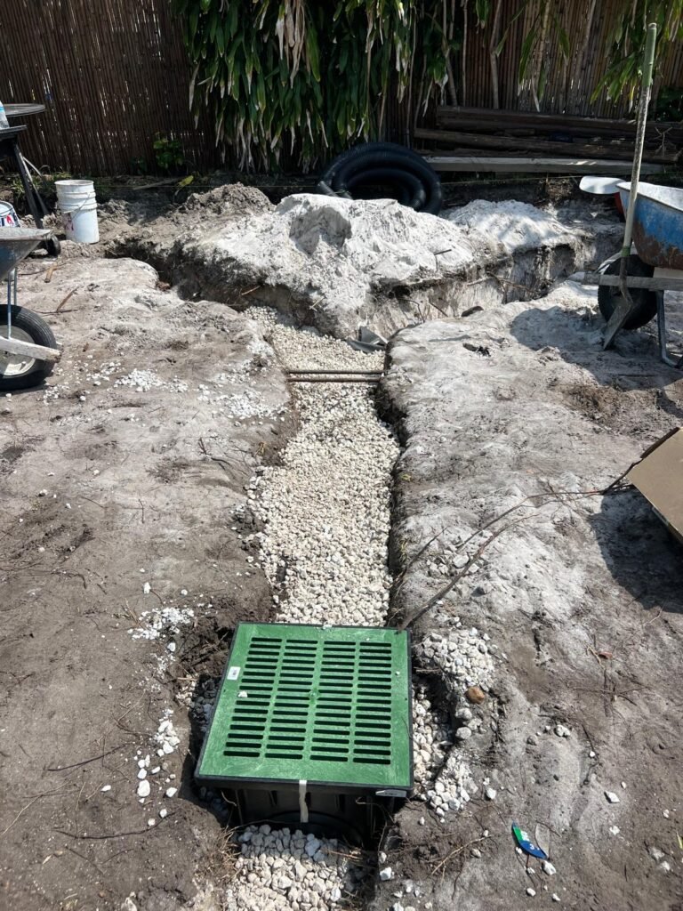 French drain trench with gravel and a green catch basin grate