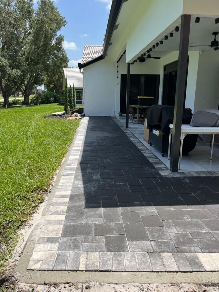 Charcoal paver patio extension with a light border beside a covered lanai