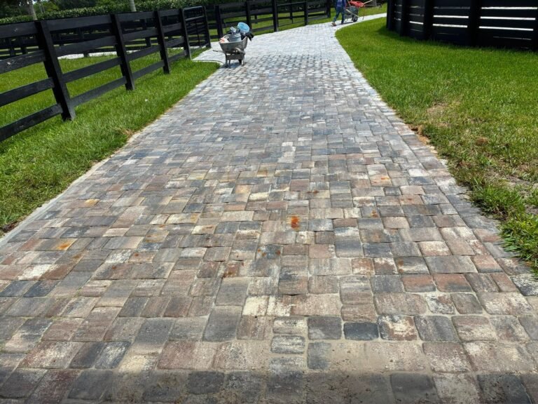 Long tumbled paver walkway running beside a black four-board ranch fence