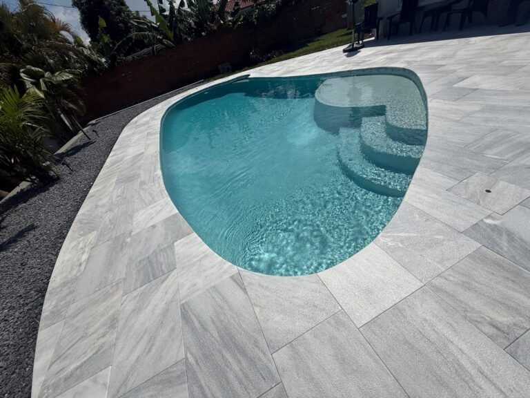 Gray porcelain pavers around a freeform pool with built-in steps
