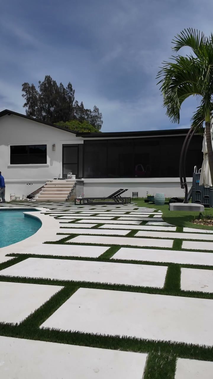 Oversized white pavers with artificial turf joints around a backyard pool in Boynton Beach, FL